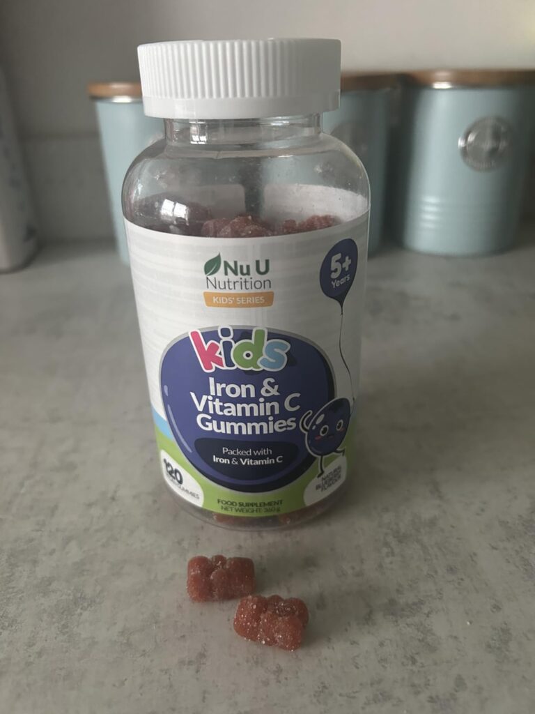 Bouteille de vitamines pour enfants, avec deux gommes à l'extérieur, posée sur une table de cuisine. Similaire au visuel 0.