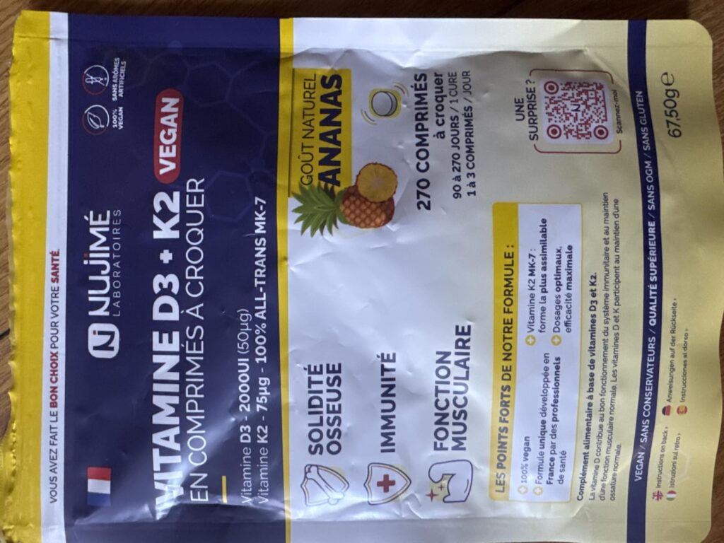 Vue d'ensemble du sachet de vitamines posé sur une table en bois. Le sachet est en plastique et présente une étiquette coloré...