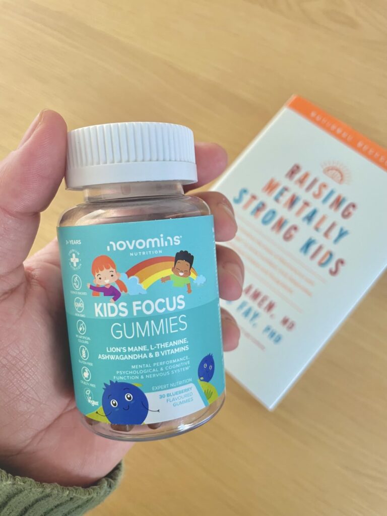 Une main tenant le flacon de Novomins Kids Focus Gummies, avec un livre en arrière-plan.