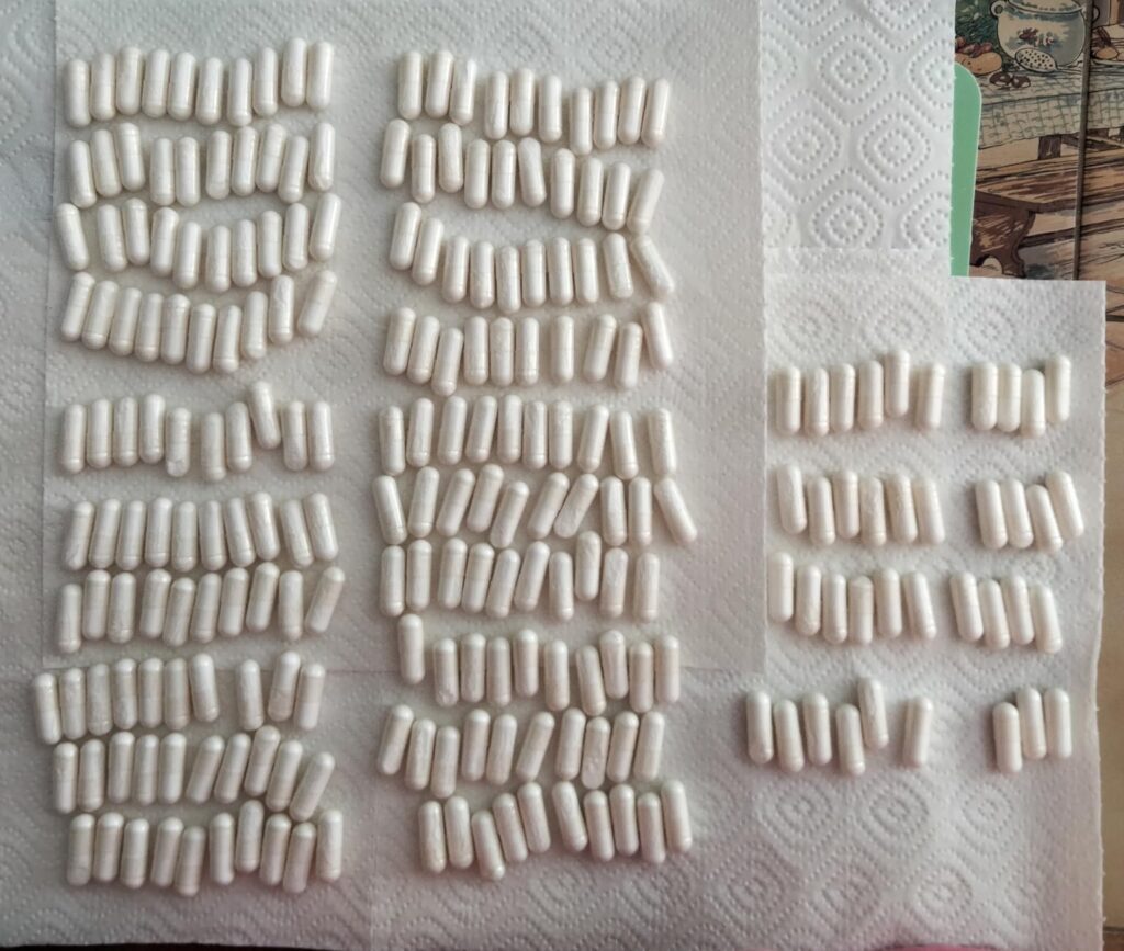 Des centaines de gélules blanches sont étalées sur une serviette en papier, regroupées en tas.