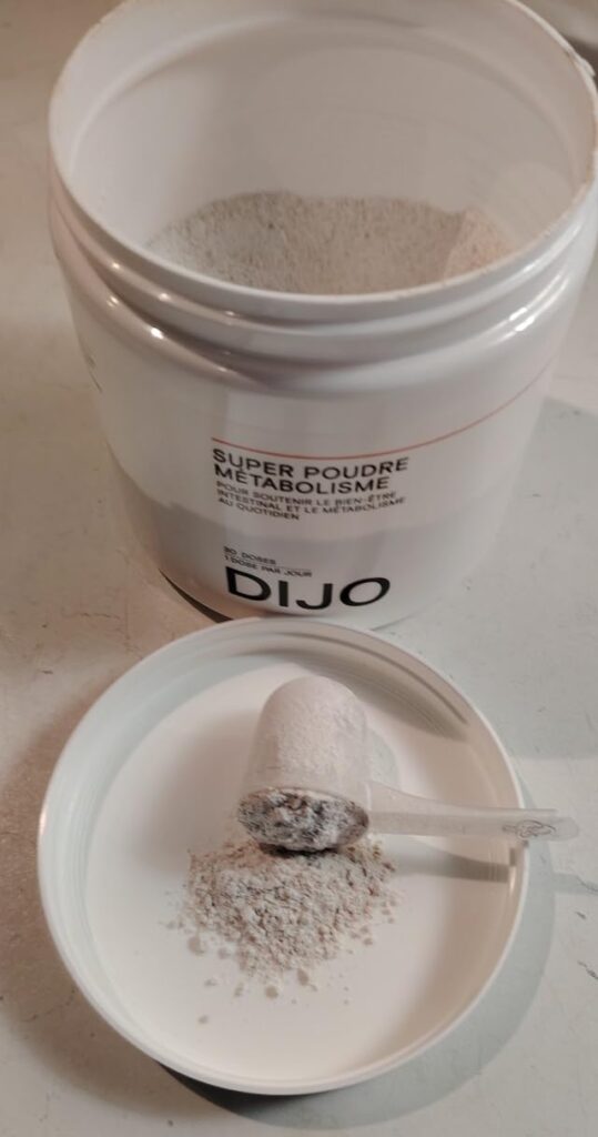 Vue en plongée du pot ouvert, avec une cuillère doseuse remplie de poudre de complément alimentaire, et une petite quantité d...