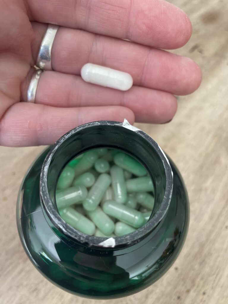 Bouteille de compléments alimentaires avec une capsule tenue dans une main.