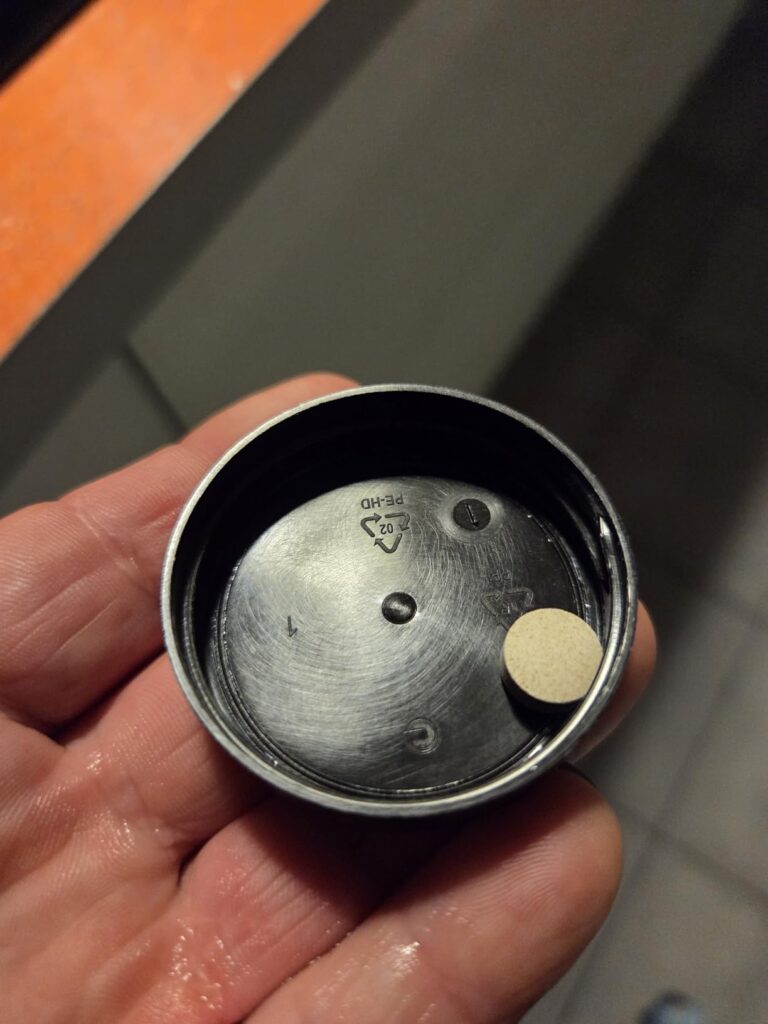 Une pastille est posée dans le couvercle de la bouteille. Le couvercle est noir et on voit une main.