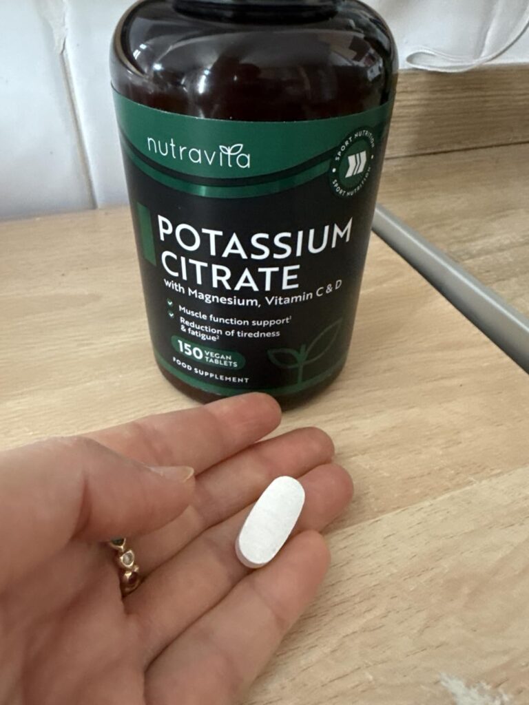 Flacon de compléments alimentaires Nutravita Potassium Citrate, une gélule blanche est posée dans la main au premier plan.