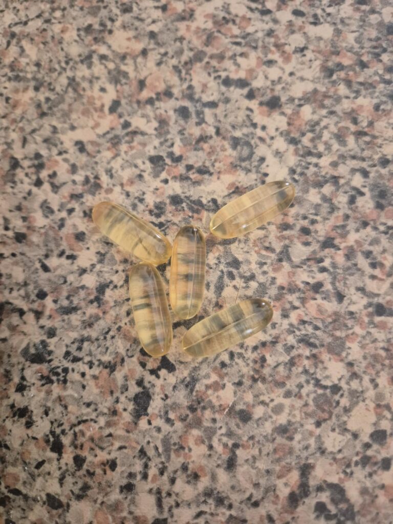 Cinq gélules d'Omega 3-6-9 de la marque Horbäach posées sur une surface marbrée.