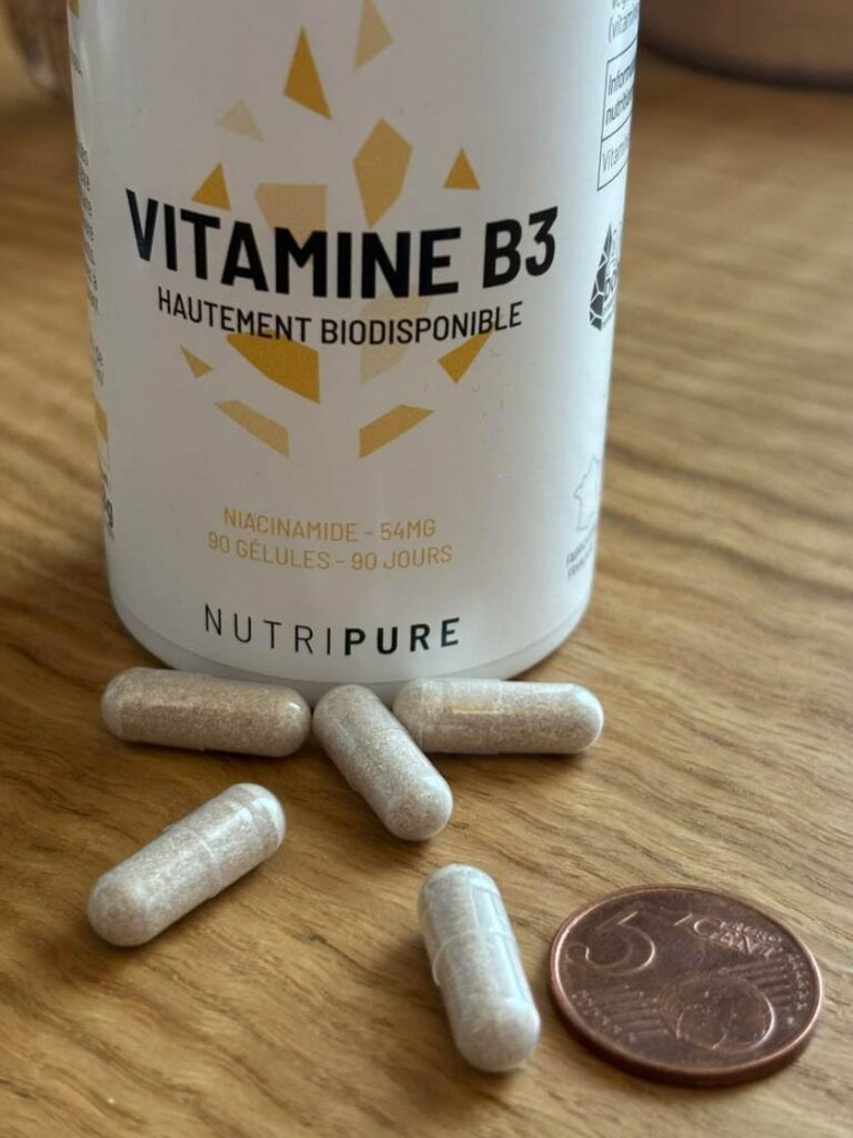 Flacon de Vitamine B3 et quelques gélules posées à côté, avec une pièce de 5 centimes pour donner l'échelle.