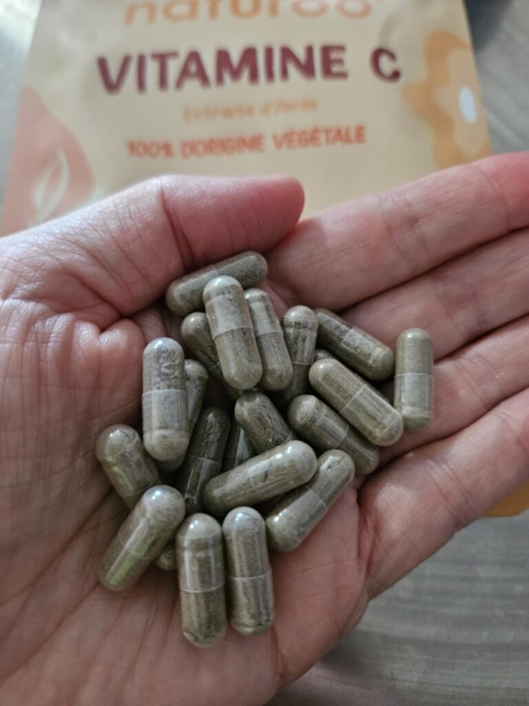 Des gélules de Vitamine C dans une main, avec le sachet en arrière-plan.