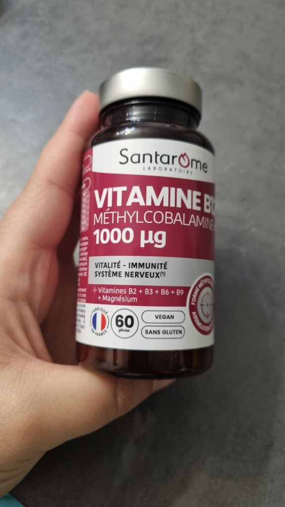 Flacon de complément alimentaire Santarome Vitamine B12 tenu dans une main, vue frontale légèrement en biais, similaire au vi...