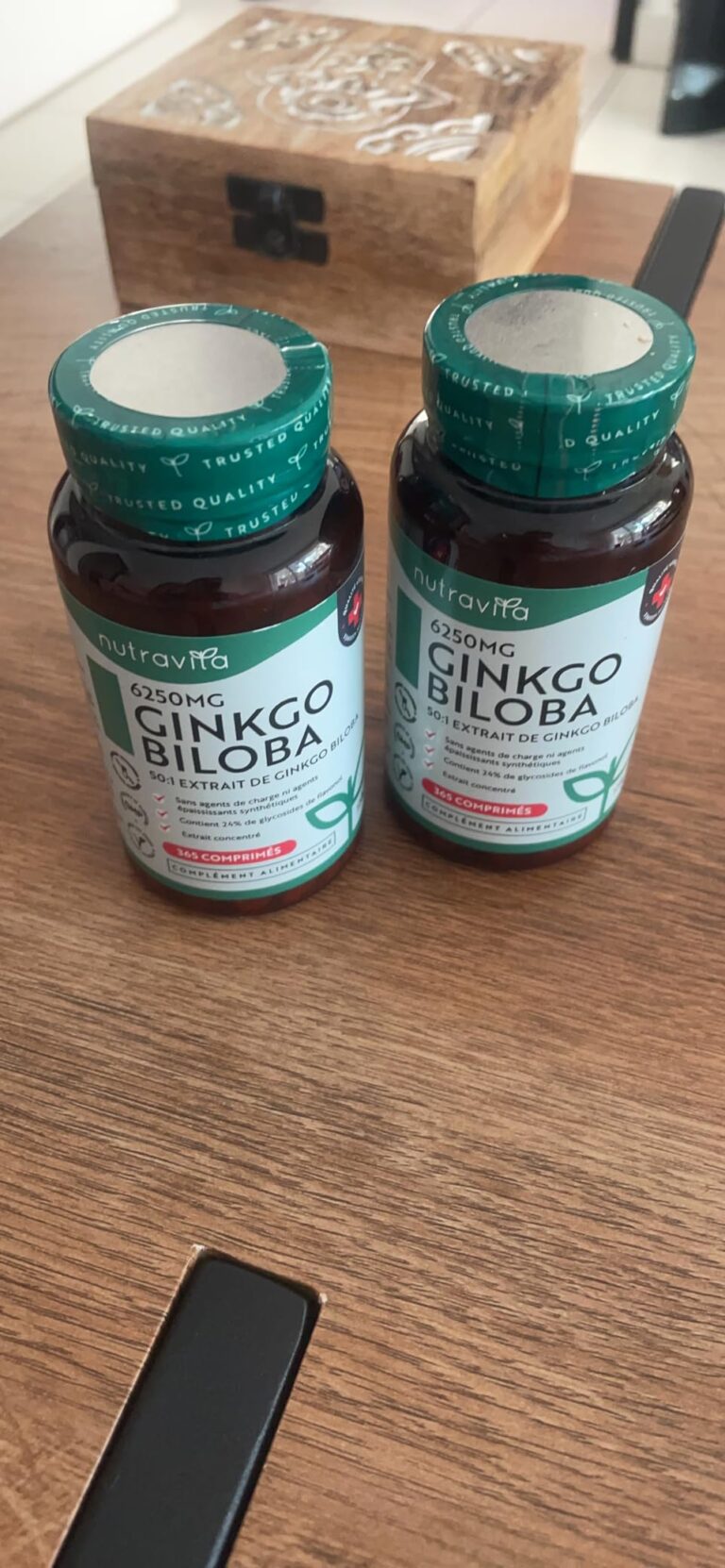 Deux flacons de Ginkgo Biloba sur une table en bois, partiellement recouverte par une boîte en bois décorée.