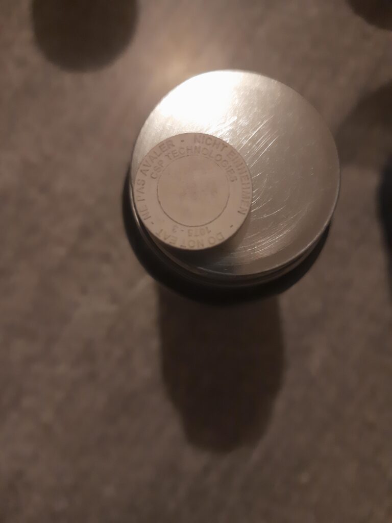 Un composant rond en métal avec un autre élément rond plus petit posé dessus, sur un fond uni et sombre.