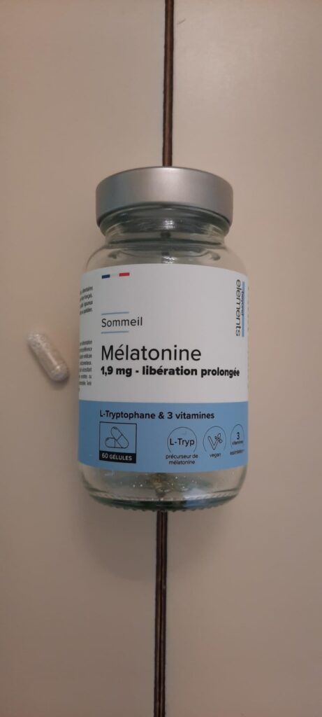 Flacon de mélatonine sur fond de mur clair, avec une gélule à côté.