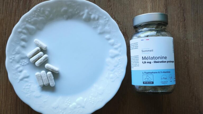 Flacon de mélatonine et plusieurs gélules sur une assiette blanche, posés sur une table en bois.