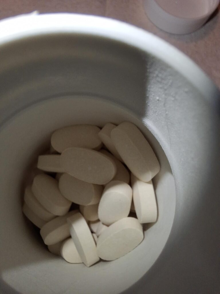 Une vue de dessus d'un pot blanc rempli de pilules blanches, identiques à celles des visuels précédents.